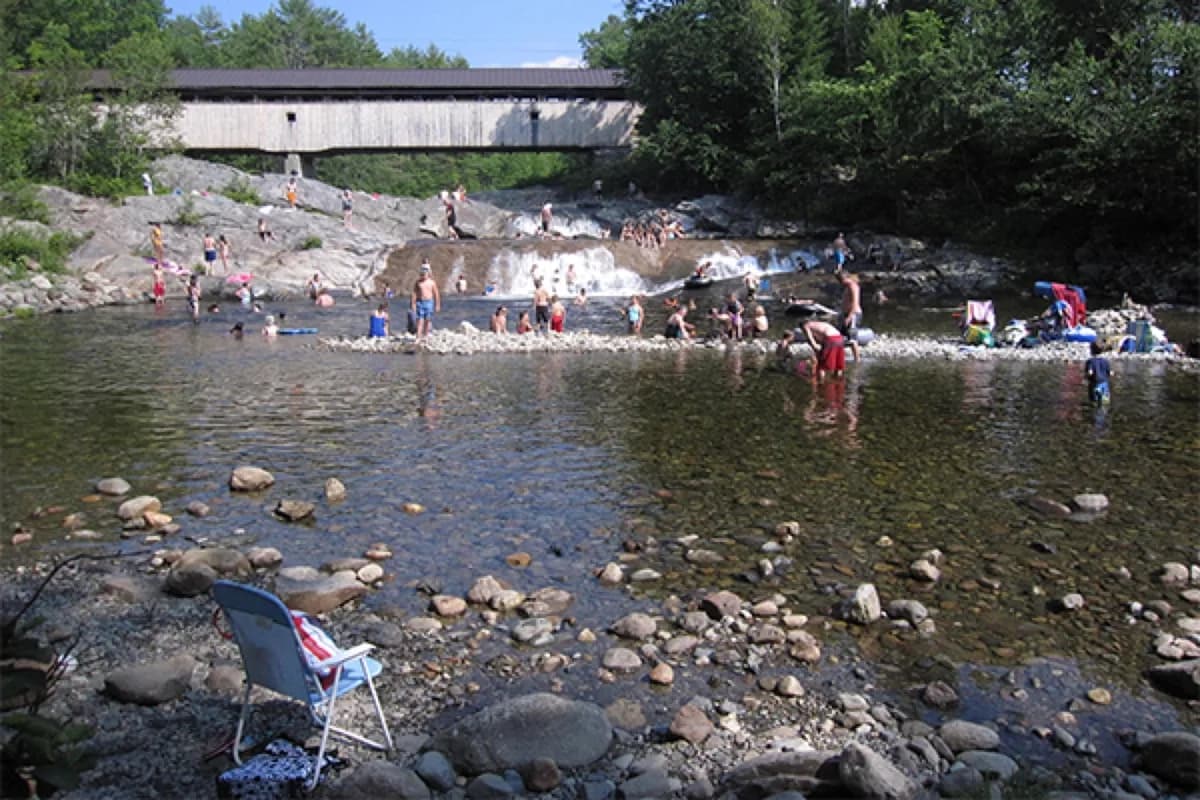 New England covered bridge over a river with a quiet swim pool underneath on a clear summer morning.