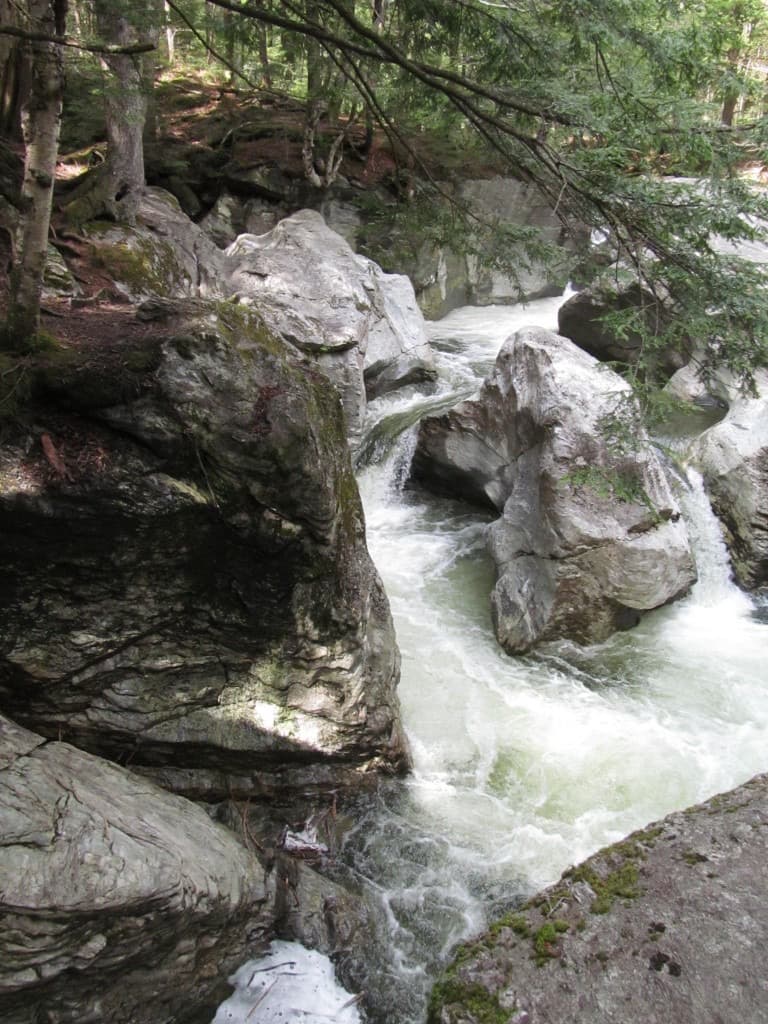 White water rushing between massive gray boulders in a narrow, forest-framed gorge at Bingham Falls.