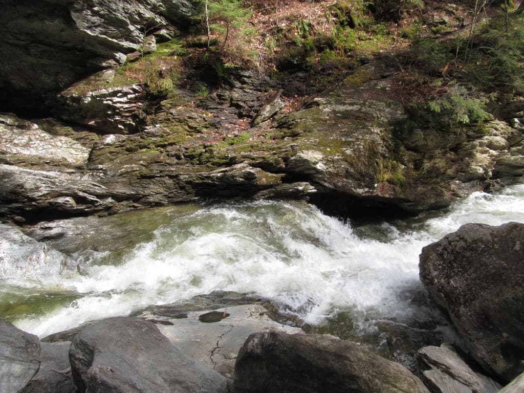 Whitewater rapids in a tight gorge with mossy, horizontally layered rock walls at Bingham Falls.