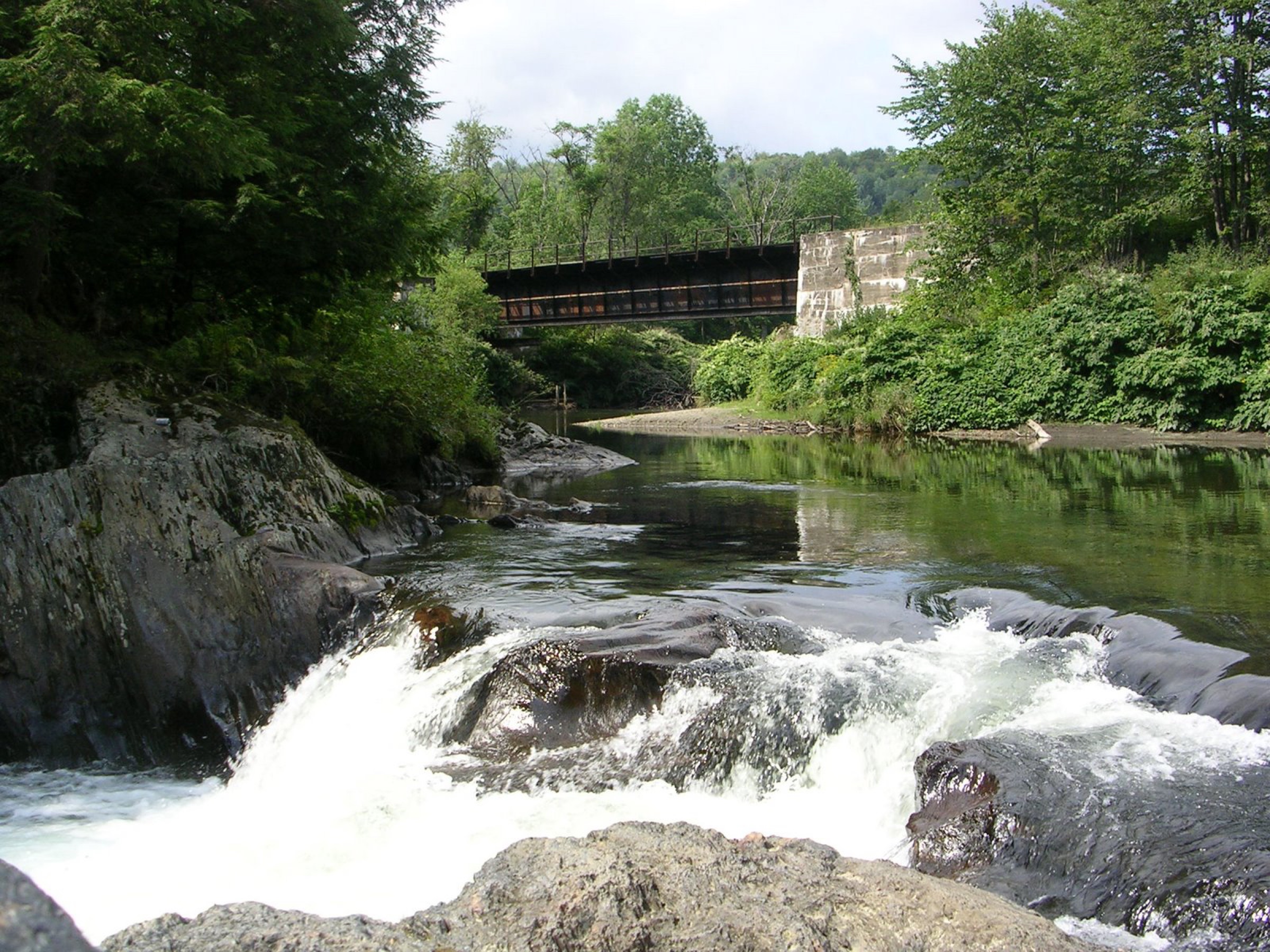 Small waterfall and plunge pool at Dog River Jacuzzi Natural Area in Berlin, Vermont, with rock walls and whitewater below a bridge.