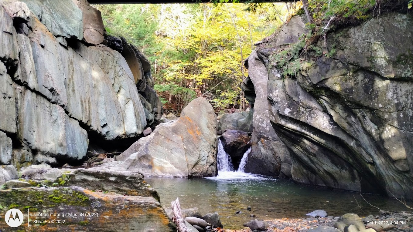 Gold Brook pool framed by steep rock walls and a small waterfall under the bridge in Stowe, Vermont.